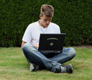 Teenage boy with wireless laptop accessing Web from garden